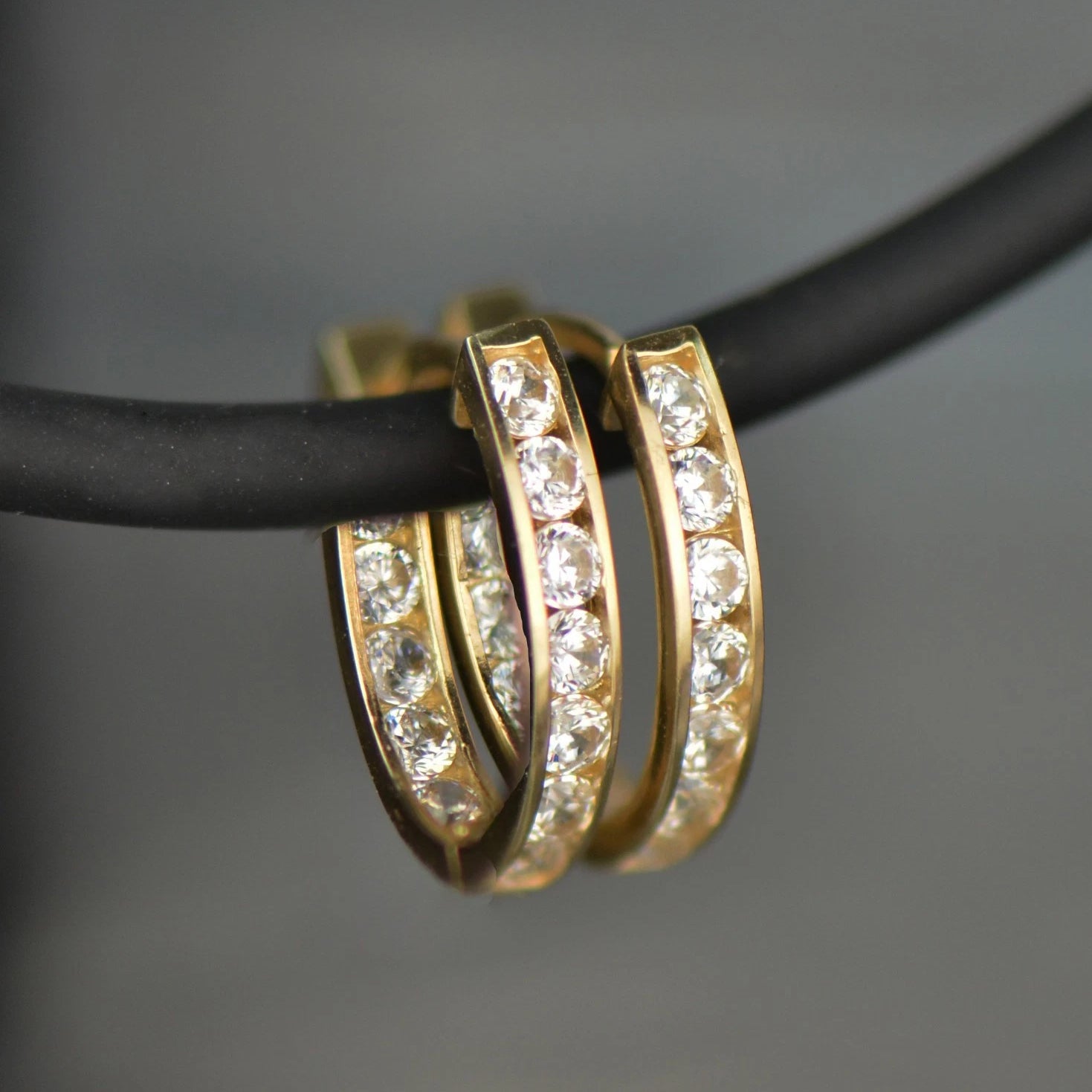 Gold hoop earrings with clear stones on a black cord against a gray background
