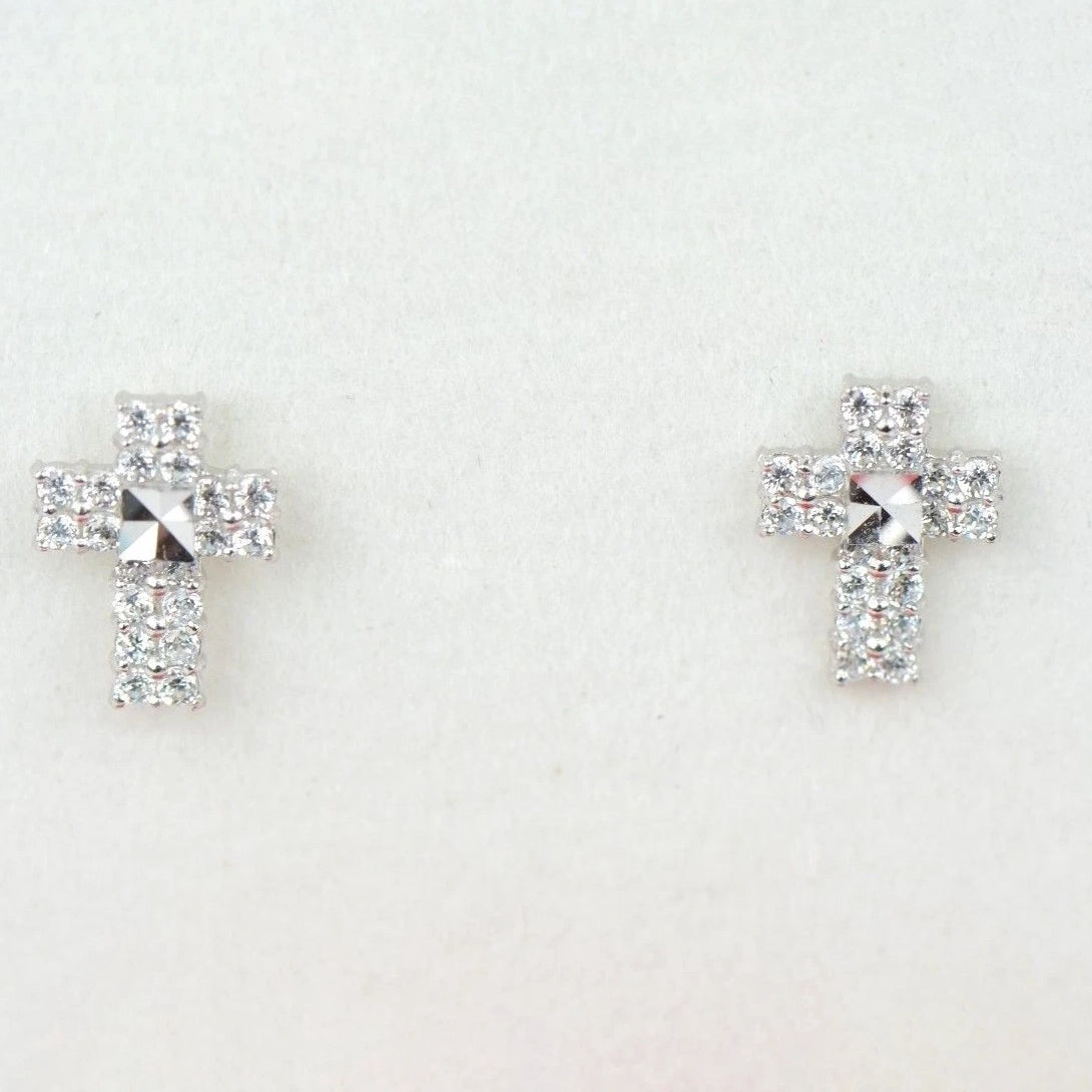 Pair of cross-shaped earrings with clear gemstones on a light gray background